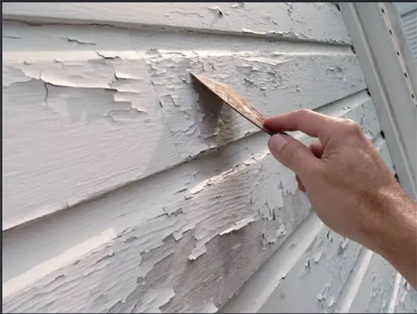 A painter scraping loose paint from wood trim before priming.