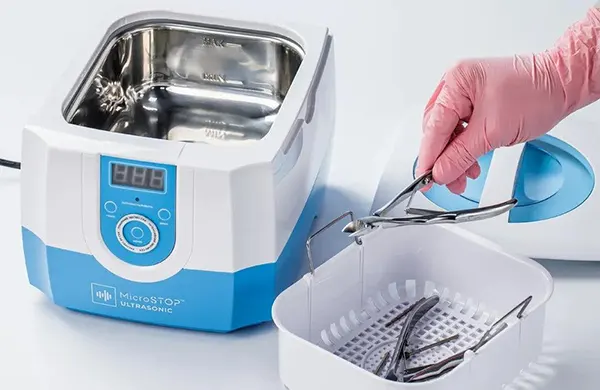 Small tabletop ultrasonic cleaner with a stainless-steel tank and removable basket on a dry work surface.