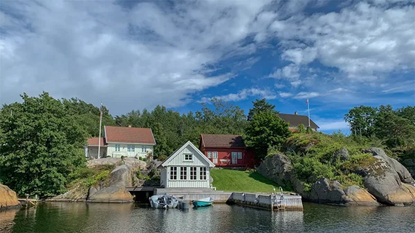 White and brown house near green trees and body of water under blue and white cloudy